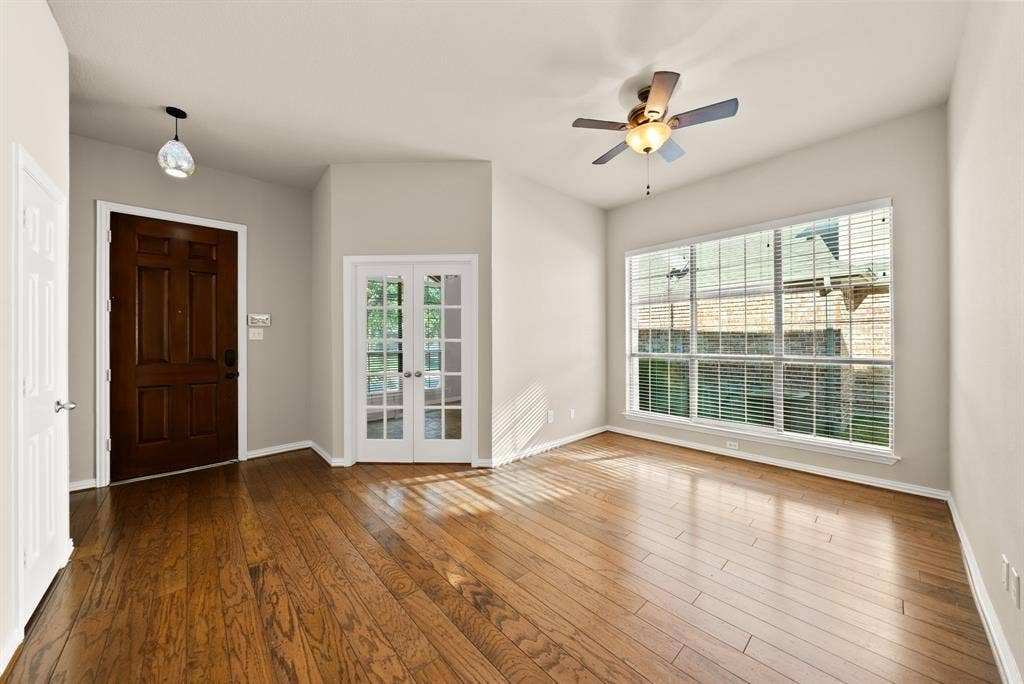 242 Cox Drive, Fate, TX 75087 Wood-finish flooring throughout, vaulted ceiling, white frame french doors, large multipane window, and a ceiling fan with integrated lighting
