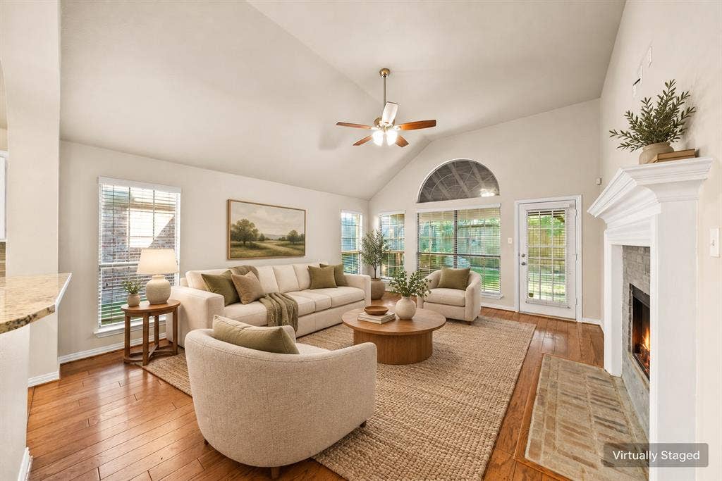 242 Cox Drive, Fate, TX 75087 Vaulted ceiling with ceiling fan, hardwood flooring, fireplace with mantel, multiple windows, and a glass-paneled exterior door
