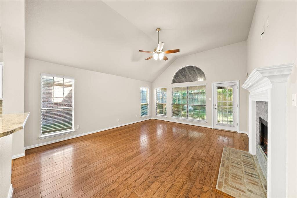 242 Cox Drive, Fate, TX 75087 Vaulted ceiling with a ceiling fan, wood-finish flooring, multiple windows, fireplace with a tiled hearth, and a glass-paneled exterior door