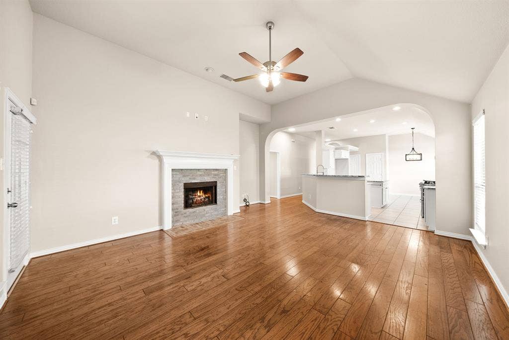 242 Cox Drive, Fate, TX 75087 Vaulted ceiling with wood-finish ceiling fan, wood-finish flooring, stone-faced fireplace with white mantel, kitchen pass-through with breakfast bar, and recessed lighting