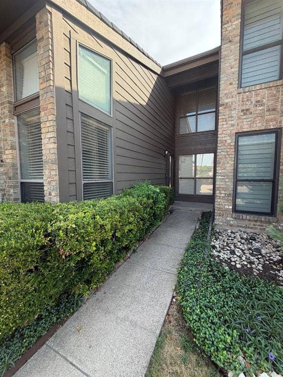 2200 W Park Boulevard, #1003, Plano, TX 75075 Exterior facade featuring horizontal siding, multi-story brick masonry columns, and tall rectangular windows with dark frames, accented by a concrete walkway and landscaped borders