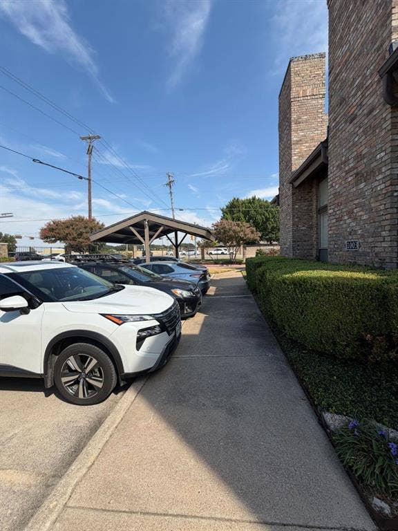 2200 W Park Boulevard, #1003, Plano, TX 75075 Brick exterior featuring a concrete walkway, manicured hedges, and a covered & open parking