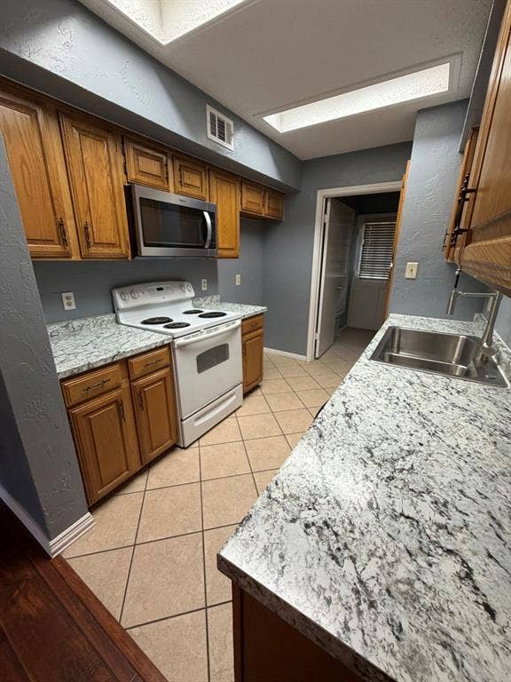 2200 W Park Boulevard, #1003, Plano, TX 75075 Kitchen featuring stone-finish countertops, wood-finish cabinetry, stainless steel sink with high-arc faucet, integrated microwave, and overhead skylight