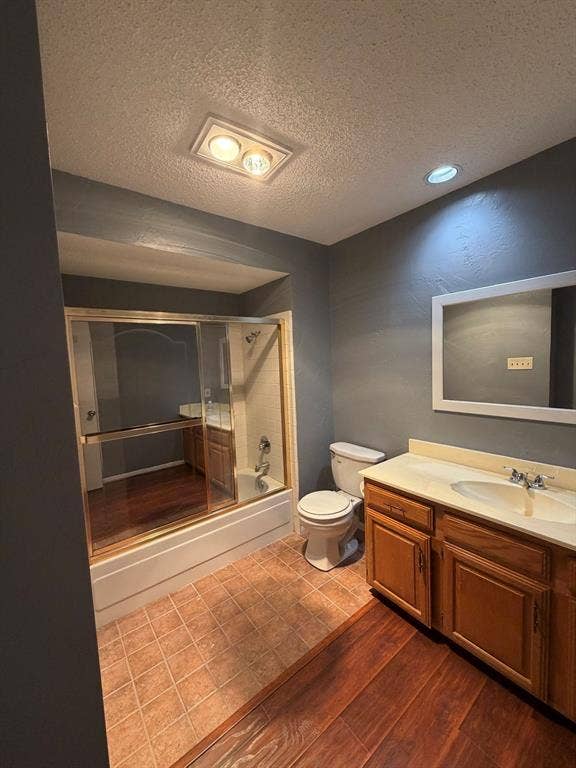 2200 W Park Boulevard, #1003, Plano, TX 75075 Bathroom featuring wood-finish cabinetry, a white countertop with an integrated sink, a built-in tub with a sliding glass enclosure, and a wall-mounted mirror