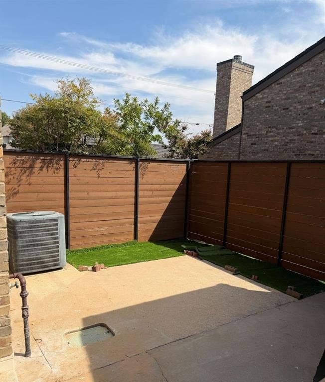 2200 W Park Boulevard, #1003, Plano, TX 75075 Outdoor space featuring horizontal wood-slat privacy fencing, concrete patio, synthetic turf, and brick exterior chimney
