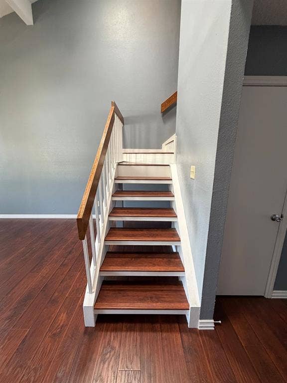 2200 W Park Boulevard, #1003, Plano, TX 75075 Staircase featuring wood-finish treads, white balusters, and a natural wood handrail, set against wood-finish flooring and high vaulted ceilings