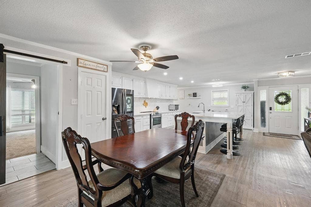 5247 Fm 1569, Farmersville, TX 75442 Open-concept living space featuring wood-finish flooring, white kitchen cabinetry, a kitchen island with seating, a ceiling fan, and a barn door entry