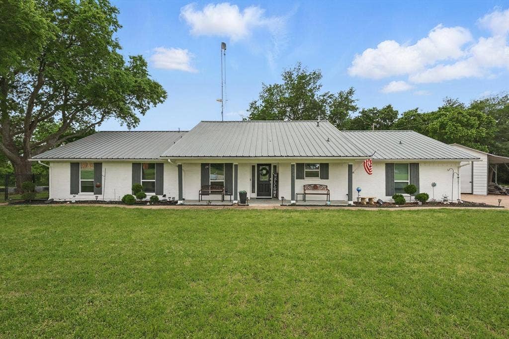 5247 Fm 1569, Farmersville, TX 75442 White brick exterior with a metal roof, covered front porch, and established landscaping