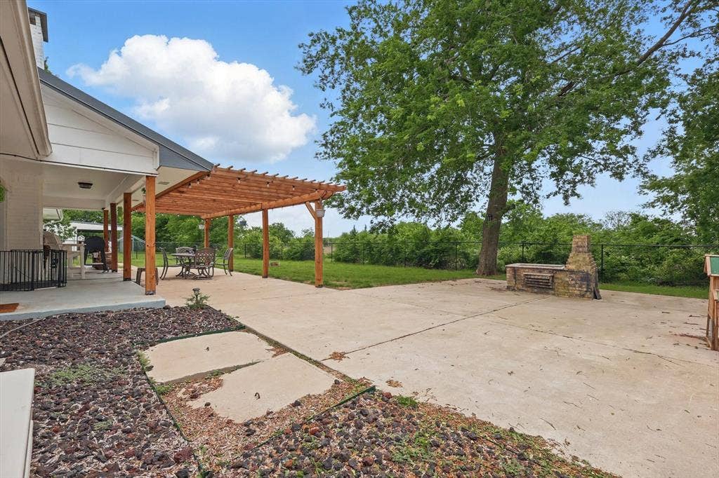 5247 Fm 1569, Farmersville, TX 75442 Expansive concrete patio with mature shade trees and open lawn space, complemented by a cedar pergola structure attached to the home