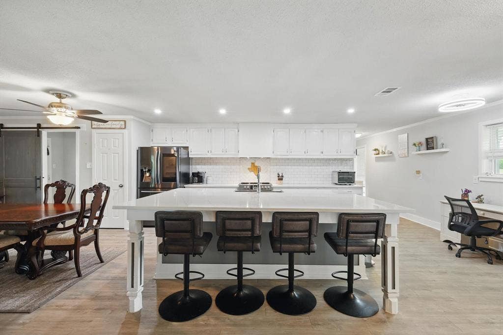 5247 Fm 1569, Farmersville, TX 75442 Open-concept kitchen and dining area featuring white cabinetry, stainless steel appliances, quartz countertops, a large waterfall-edge island with seating for four, and wood-finish flooring throughout the space