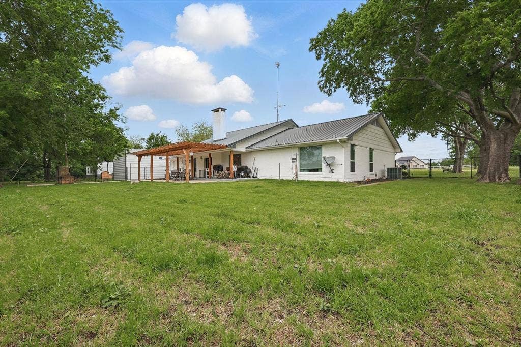 5247 Fm 1569, Farmersville, TX 75442 Expansive green space featuring a white exterior residence with a gray metal roof, a wood pergola over a concrete patio, and mature trees