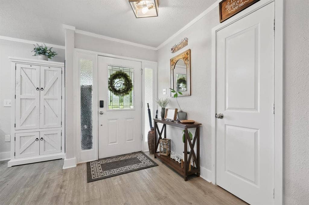 5247 Fm 1569, Farmersville, TX 75442 Welcoming foyer showcasing white six-panel doors, wood-finish flooring, geometric entry mat, and decorative wall-mounted mirrors