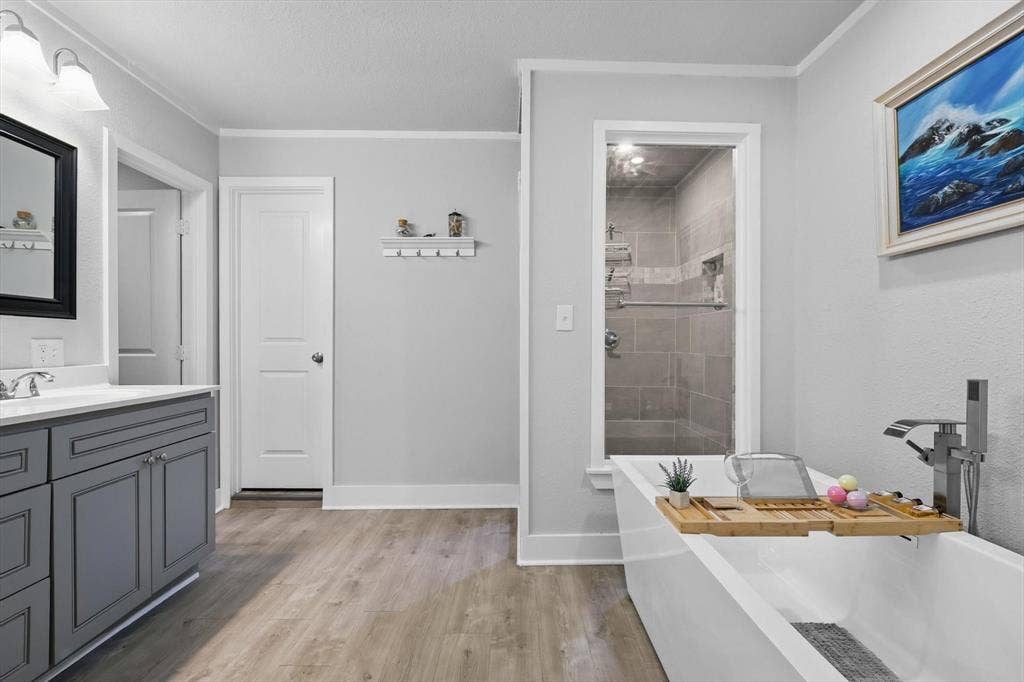 5247 Fm 1569, Farmersville, TX 75442 Spa-inspired primary bathroom featuring a freestanding soaking tub with chrome fixtures, wood-finish flooring, and a walk-in shower with tile surround