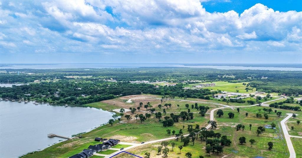 200 Caro Drive, West Tawakoni, TX 75454 Aerial perspective of waterfront parcel featuring expansive grassy terrain, mature trees, a private wooden dock, and paved road access