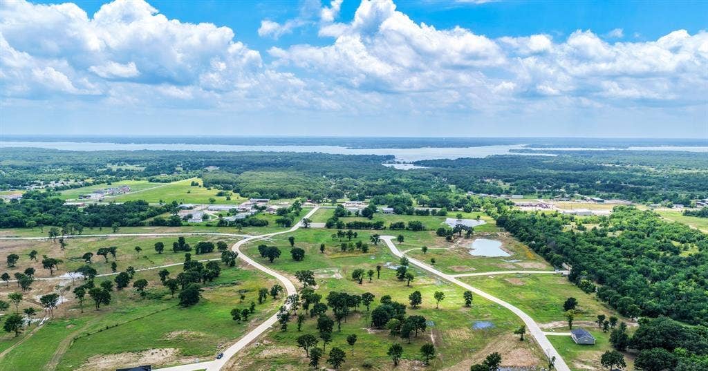200 Caro Drive, West Tawakoni, TX 75454 Expansive acreage featuring cleared pasture land, mature trees, paved roadways, and a water backdrop