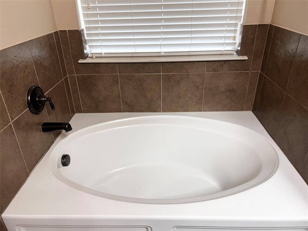5204 Bear Valley Drive, McKinney, TX 75071 Oval soaking tub with a tiled surround, oil-rubbed bronze fixtures, and white window blinds