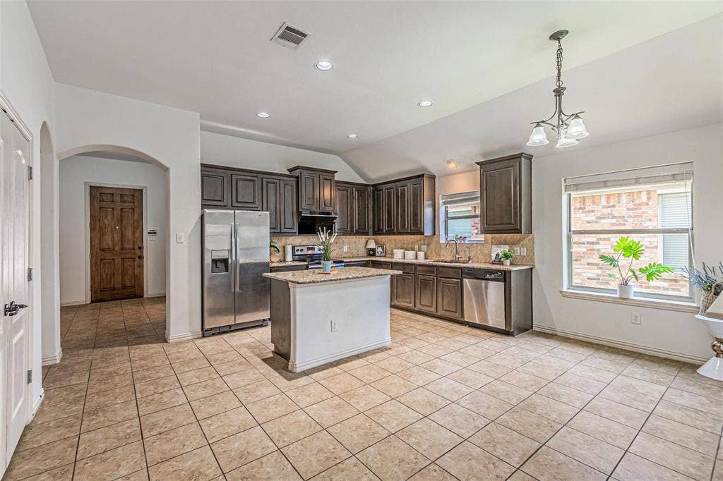 Spacious kitchen featuring dark wood cabinetry, stainless steel appliances, a center island with granite-style countertop, and tile flooring
