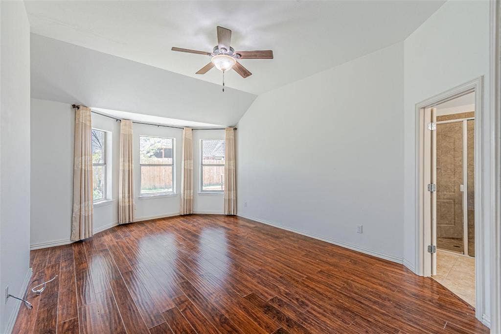 Spacious room with wood-finish flooring, vaulted ceiling, and a ceiling fan