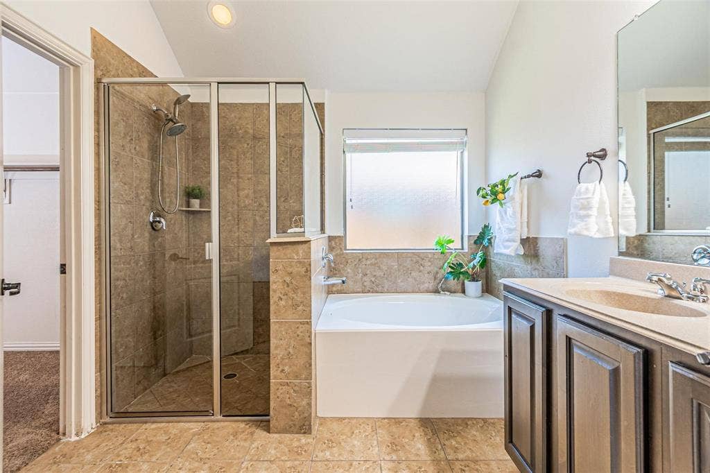 Expansive tile flooring, separate shower with glass enclosure, built-in bathtub, and a double vanity with an integrated sink