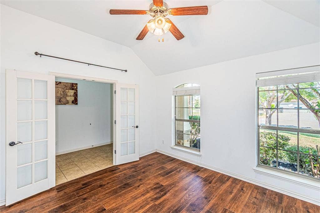 Vaulted ceiling with a ceiling fan, wood-finish flooring, two large windows, an arched window, and double French doors