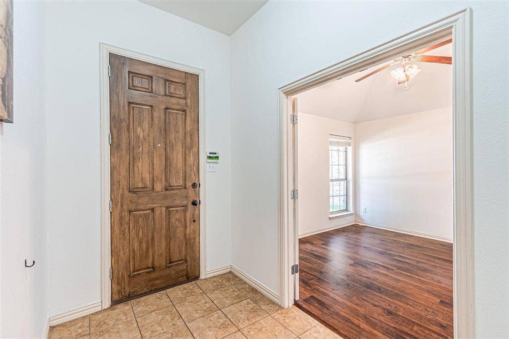 Wood-finish entry door, tiled flooring, cased doorway, vaulted ceiling, and wood-finish flooring