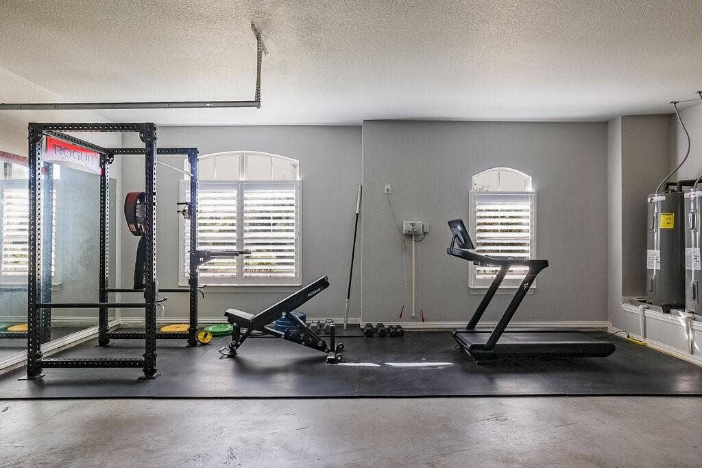 Poured concrete flooring, arched windows with plantation shutters, mirrored wall, and wall-mounted water heaters