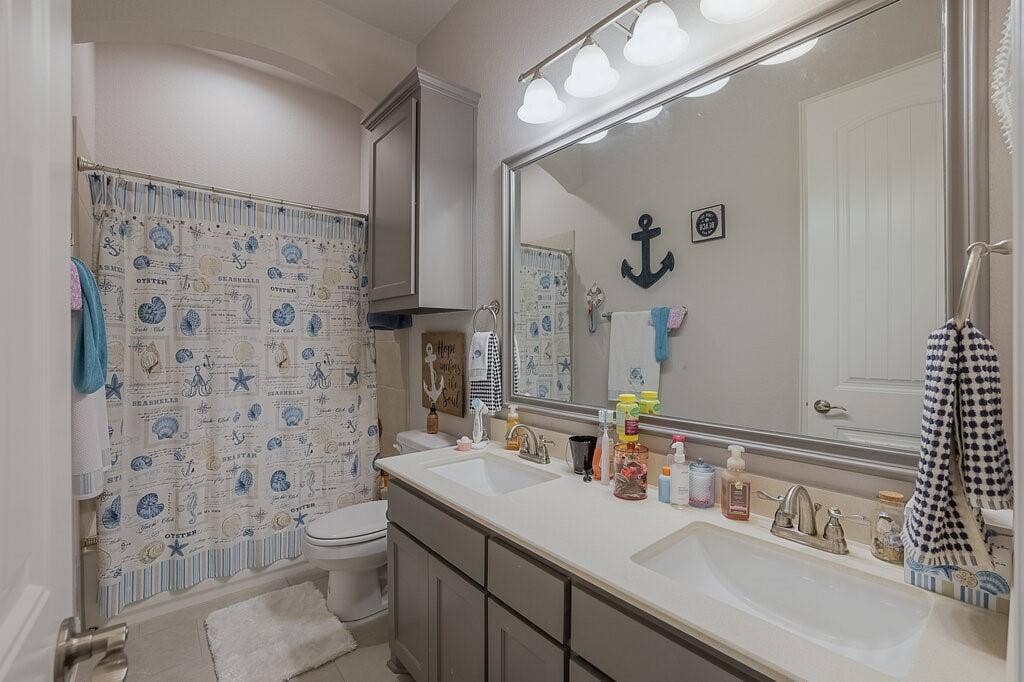 Double vanity with integrated sinks and brushed nickel faucets, large wall-mounted mirror, overhead vanity lighting, and built-in cabinetry