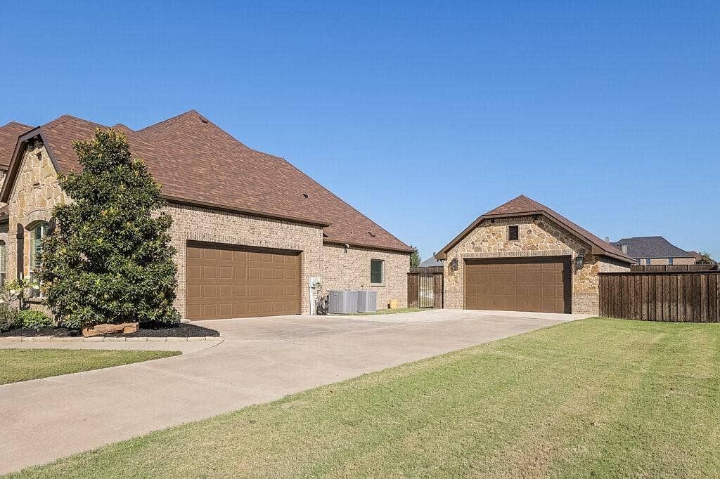 Stone and brick exterior with a multi-car garage, separate detached garage, composition shingle roofing, and a concrete driveway