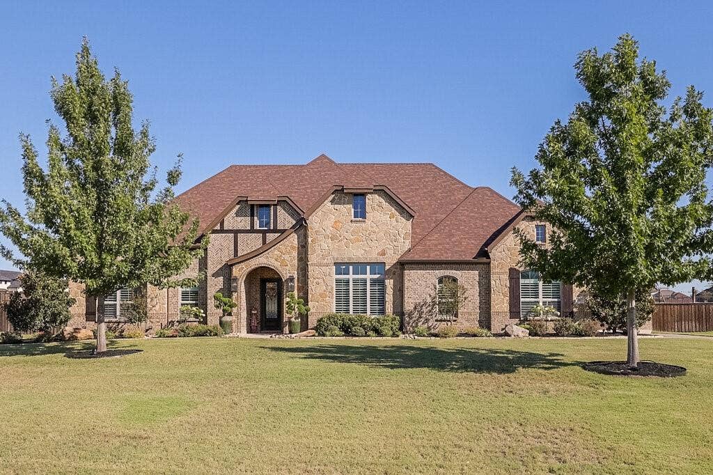 Stone and timber-frame exterior detailing, arched entryway, multi-pane windows with shutters, and a shingle roof