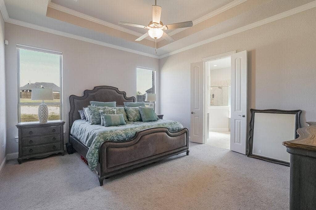 Tray ceiling with crown molding, ceiling fan with integrated lighting, recessed windows with trim, and a double-door entry