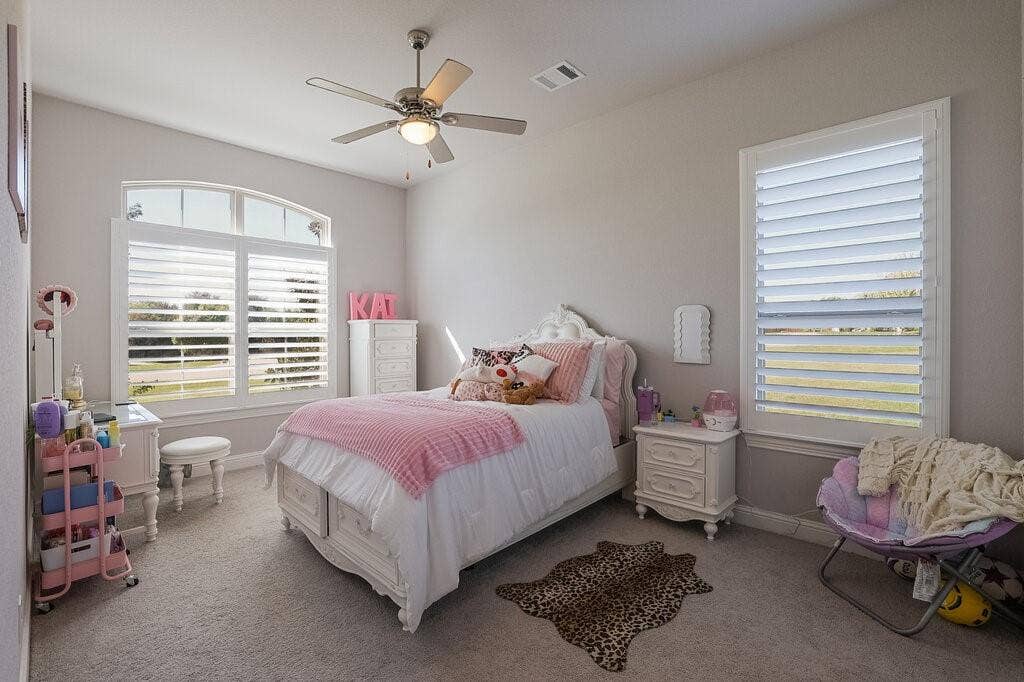 Recessed lighting, ceiling fan with integrated light, arched window, plantation shutters, and light-colored carpeting