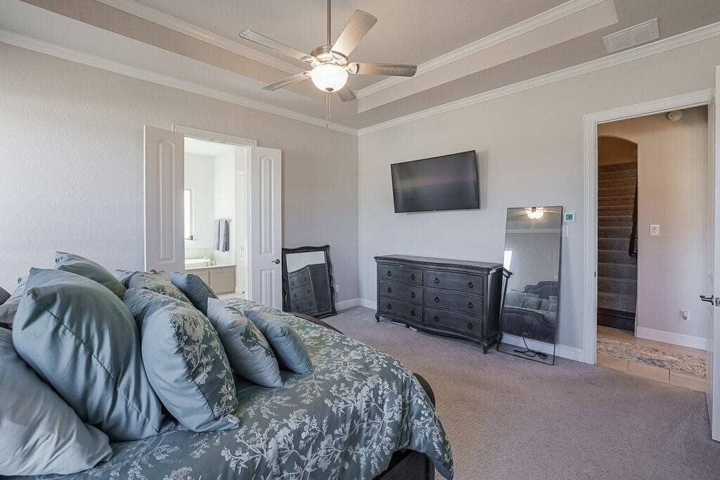 Tray ceiling with crown molding, ceiling fan with light fixture, carpeted flooring, and double-door entry to bathroom