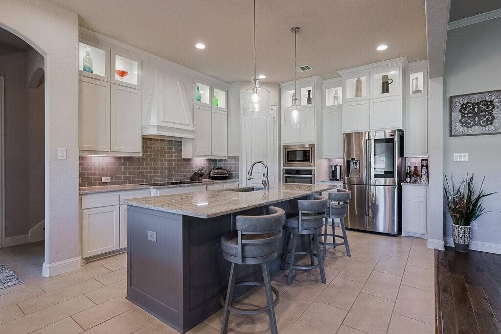 Kitchen featuring a large island with seating, pendant lighting, stainless steel appliances, white cabinetry, and a subway tile backsplash
