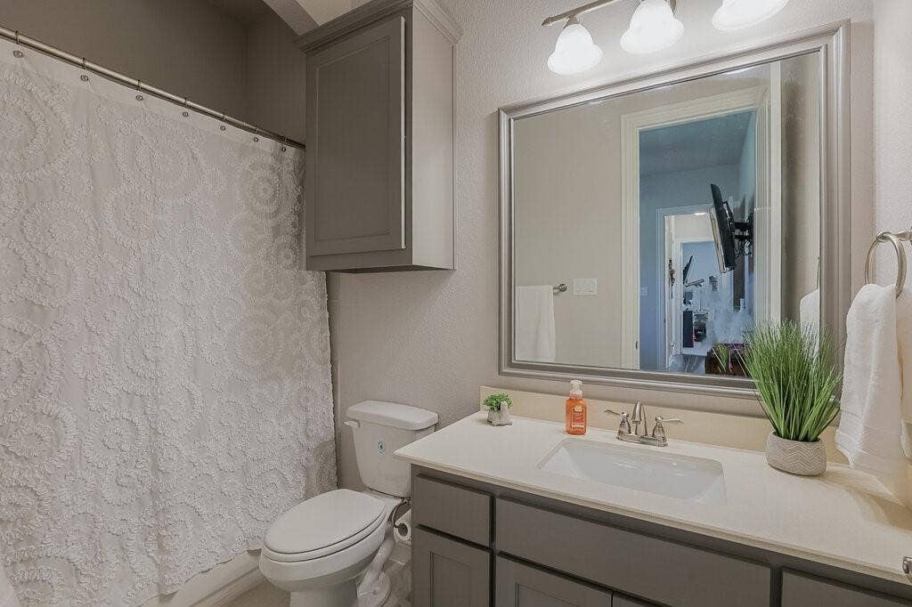 Bathroom featuring a vanity with an integrated sink, framed mirror, wall-mounted light fixture, and overhead cabinetry