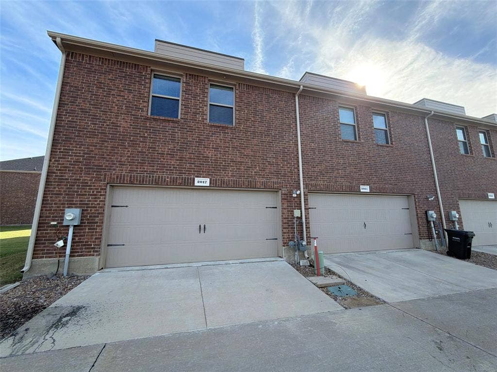 Multi-story brick exterior featuring attached dual-car garages, concrete driveways, and rectangular windows