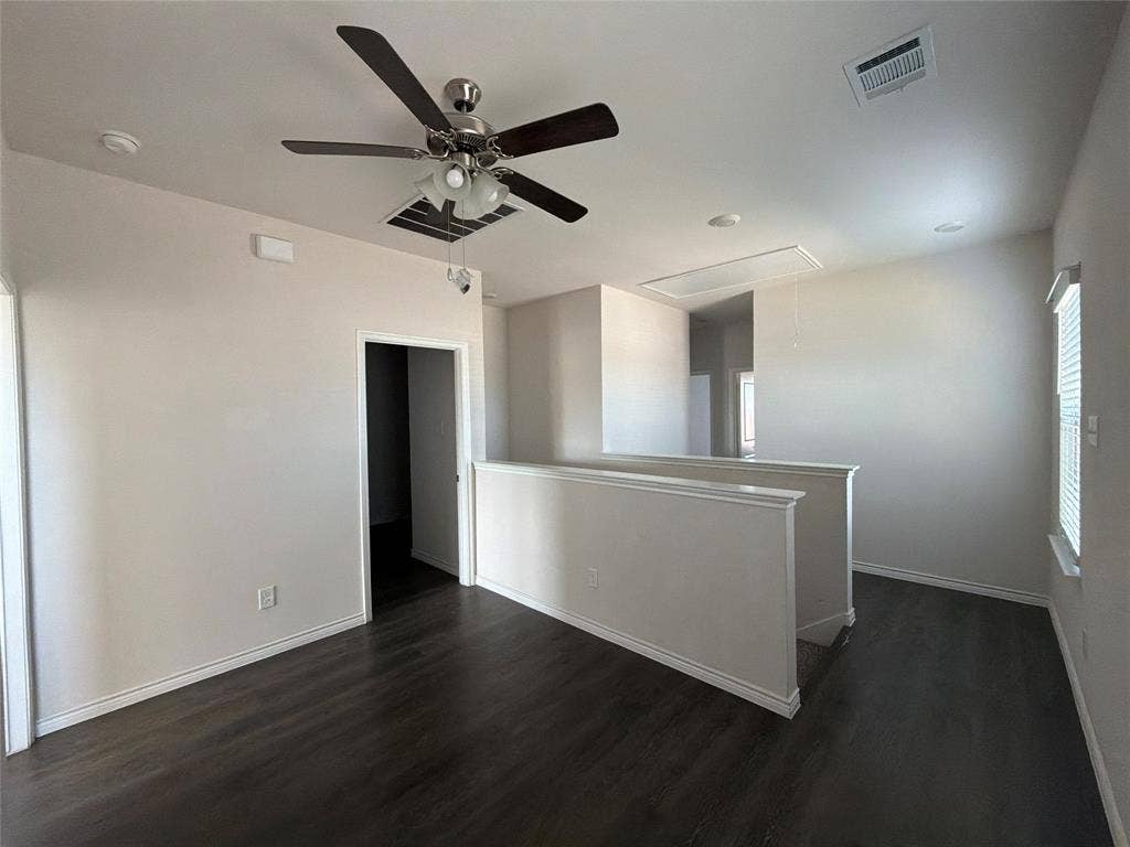 Open-concept space featuring dark wood-finish flooring, a multi-blade ceiling fan with integrated lighting, neutral wall paint, and natural illumination provided by a side window