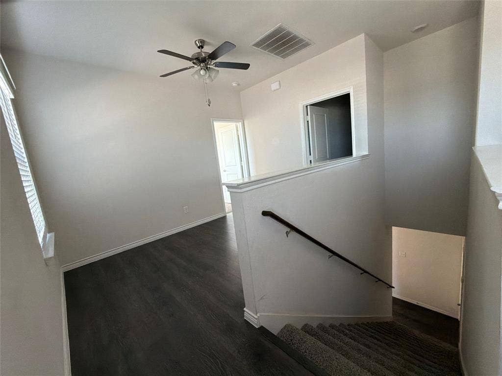 Open-concept landing featuring wood-finish flooring, a ceiling fan with integrated lighting, carpeted stairs, and a dark-finish handrail