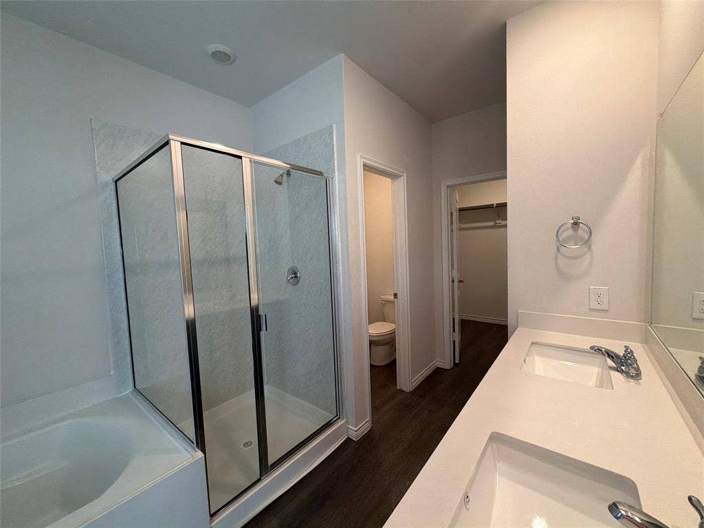 Dual-sink vanity with quartz countertop, walk-in shower with glass enclosure, separate soaking tub, and dark wood-finish flooring