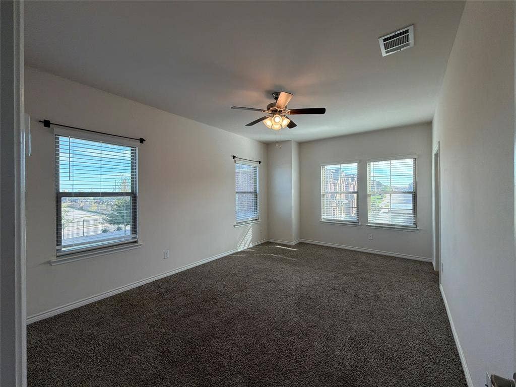 Neutral interior space featuring wall-to-wall carpeting, three windows with blinds, and a centrally mounted ceiling fan with integrated light fixture