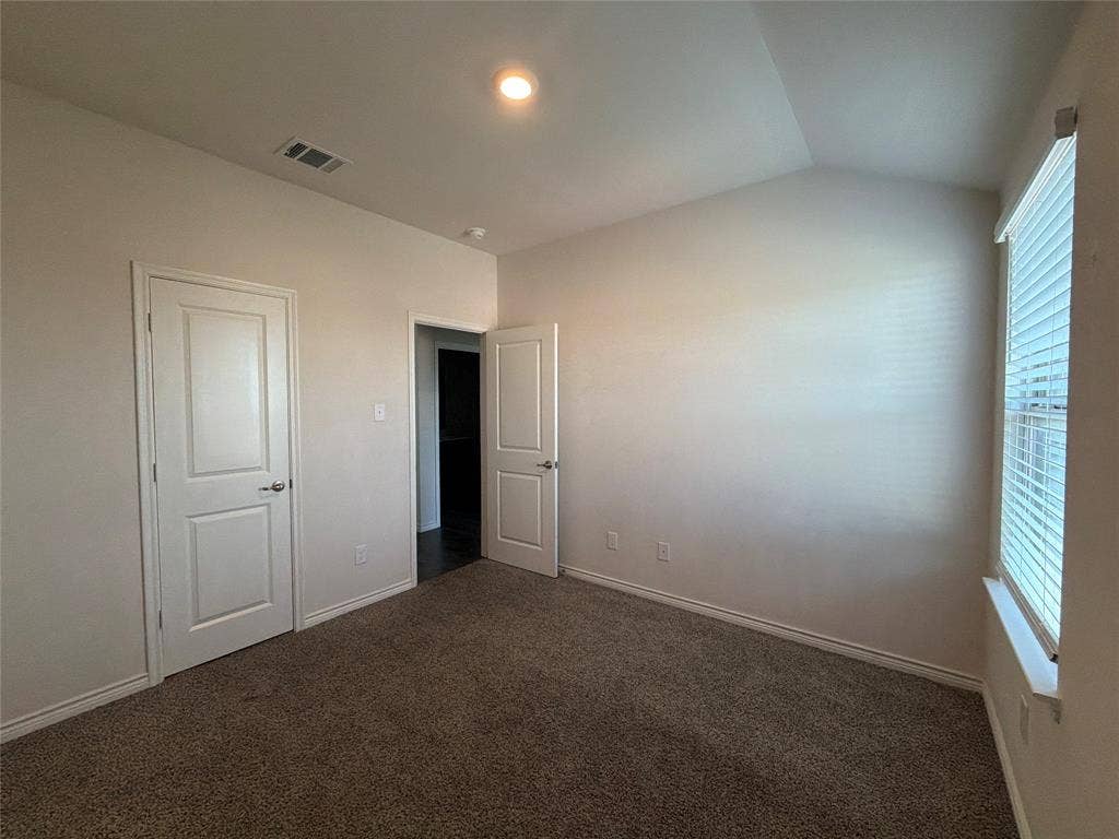 Vaulted ceiling, neutral wall tones, carpeted flooring, two interior panel doors, and window with slatted blinds