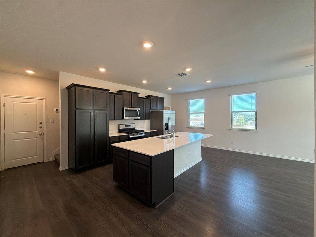 Kitchen featuring dark-finish cabinetry, white countertops, a center island with a sink, recessed lighting, and wood-finish flooring