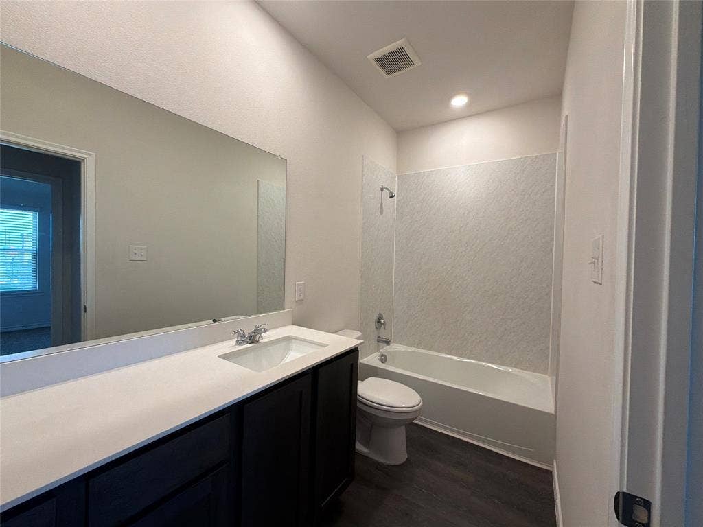 Bathroom featuring a white vanity with a rectangular undermount sink, a large wall-to-wall mirror, dark wood-finish cabinetry, and a tub-shower combination with textured wall surround