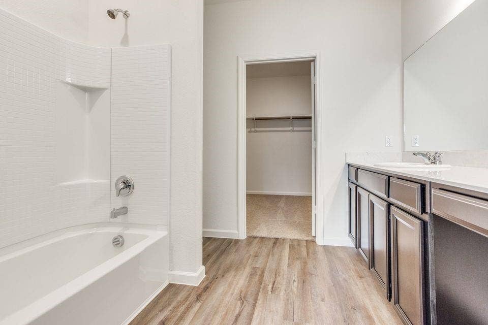212 Briar Cove, Anna, TX 75409 Tub and shower combination with white subway tile surround, wood-finish flooring, dark wood-finish vanity with countertop, and large wall-mounted mirror