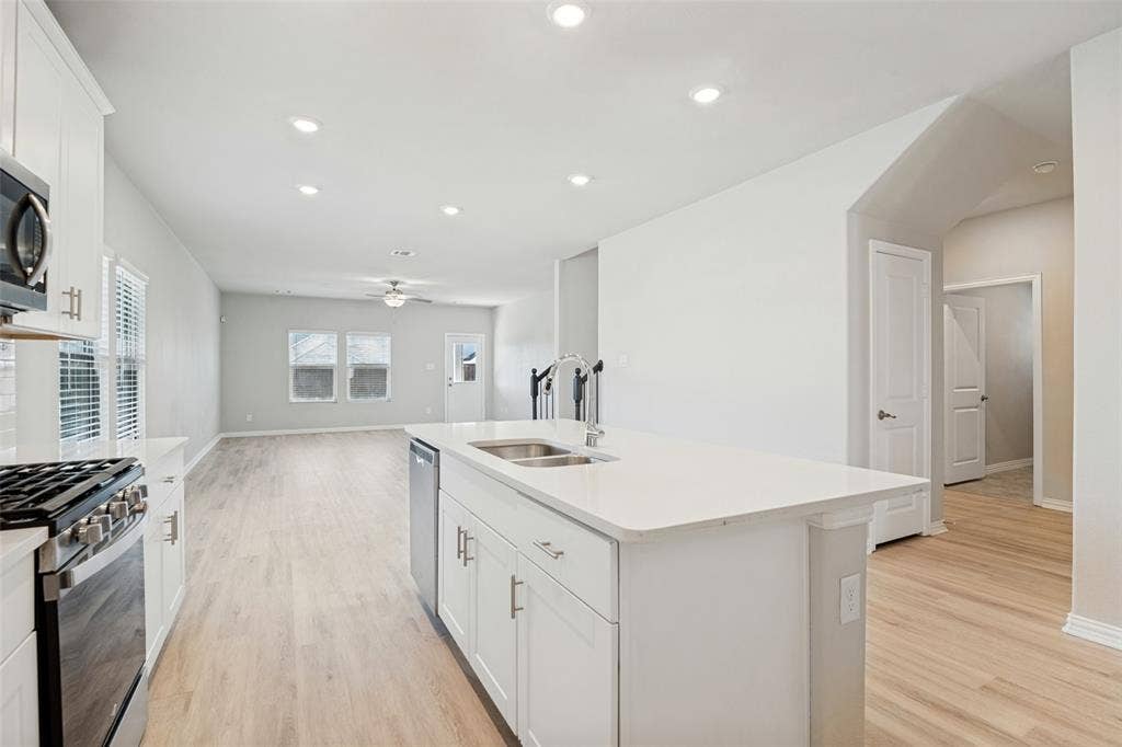 Kitchen island with a double basin sink, white cabinetry, integrated dishwasher, and light-toned wood-finish flooring throughout