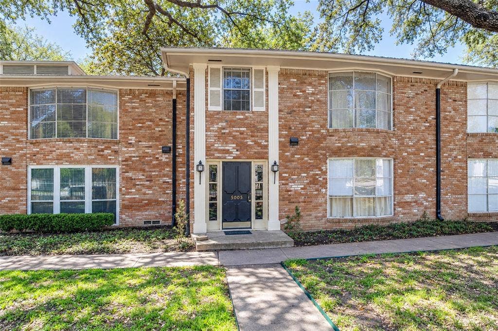5005 Cedar Springs Road, #A, Dallas, TX 75235 Brick facade featuring white trim, bay windows, a central entry with sidelights, and mature trees