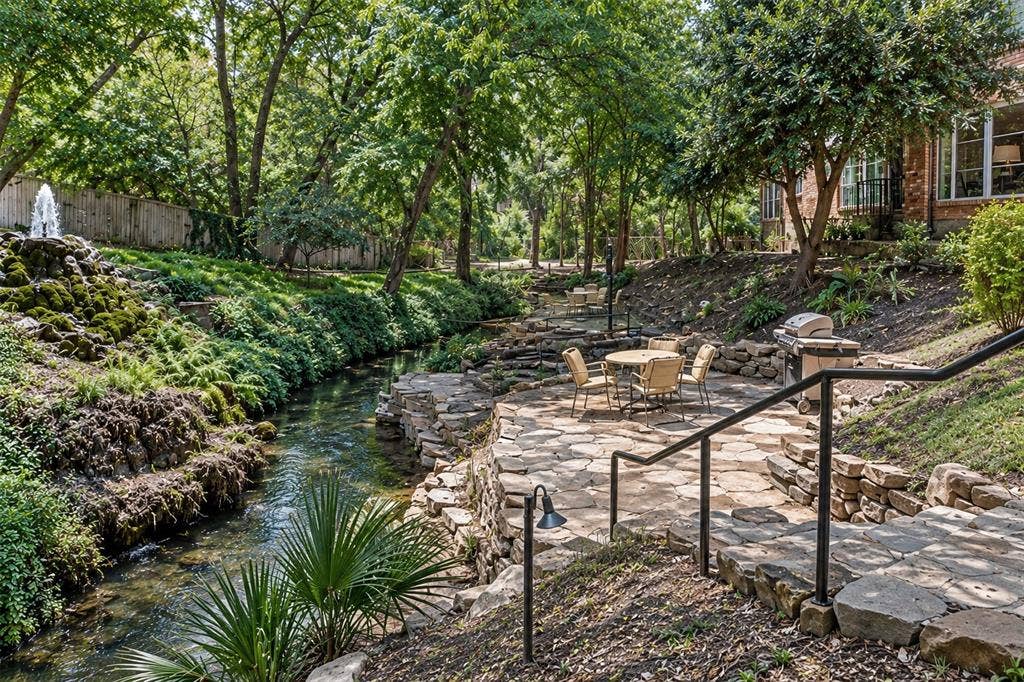 5005 Cedar Springs Road, #A, Dallas, TX 75235 Expansive outdoor space featuring a natural stream, a decorative fountain, a stone patio with a built-in grill, and mature trees