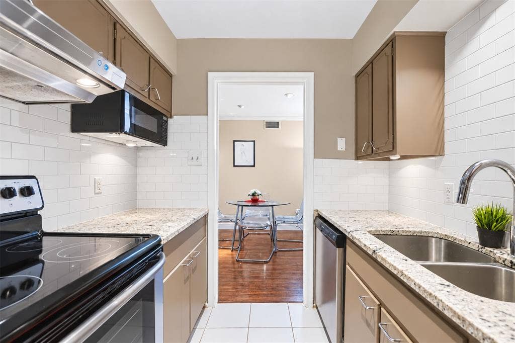 5005 Cedar Springs Road, #A, Dallas, TX 75235 Galley kitchen featuring granite countertops, a white subway tile backsplash, stainless steel appliances, and under-cabinet lighting