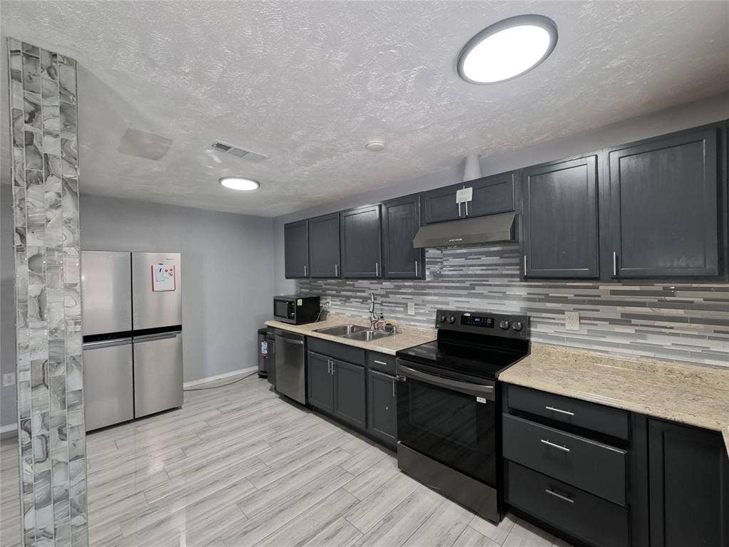 21 W Townhouse Lane, #33, Grand Prairie, TX 75052 Kitchen featuring dark cabinetry, light-toned countertops, stainless steel appliances, a tile backsplash, and wood-finish flooring