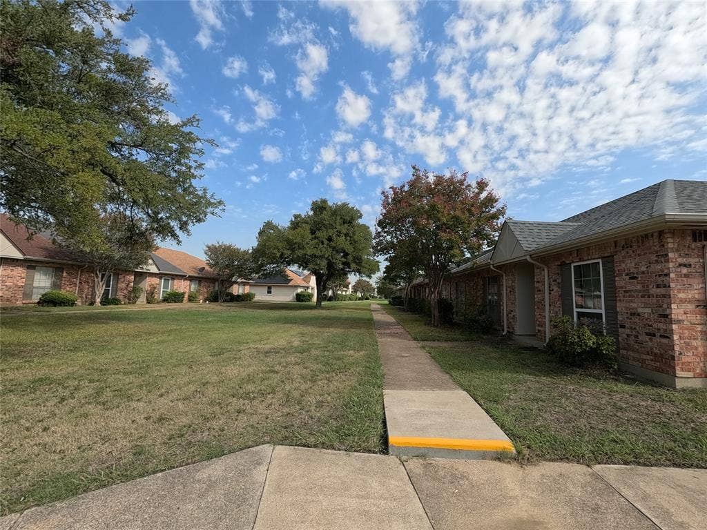 21 W Townhouse Lane, #33, Grand Prairie, TX 75052 Brick exterior residence with a gabled roofline, mature trees, and a concrete walkway