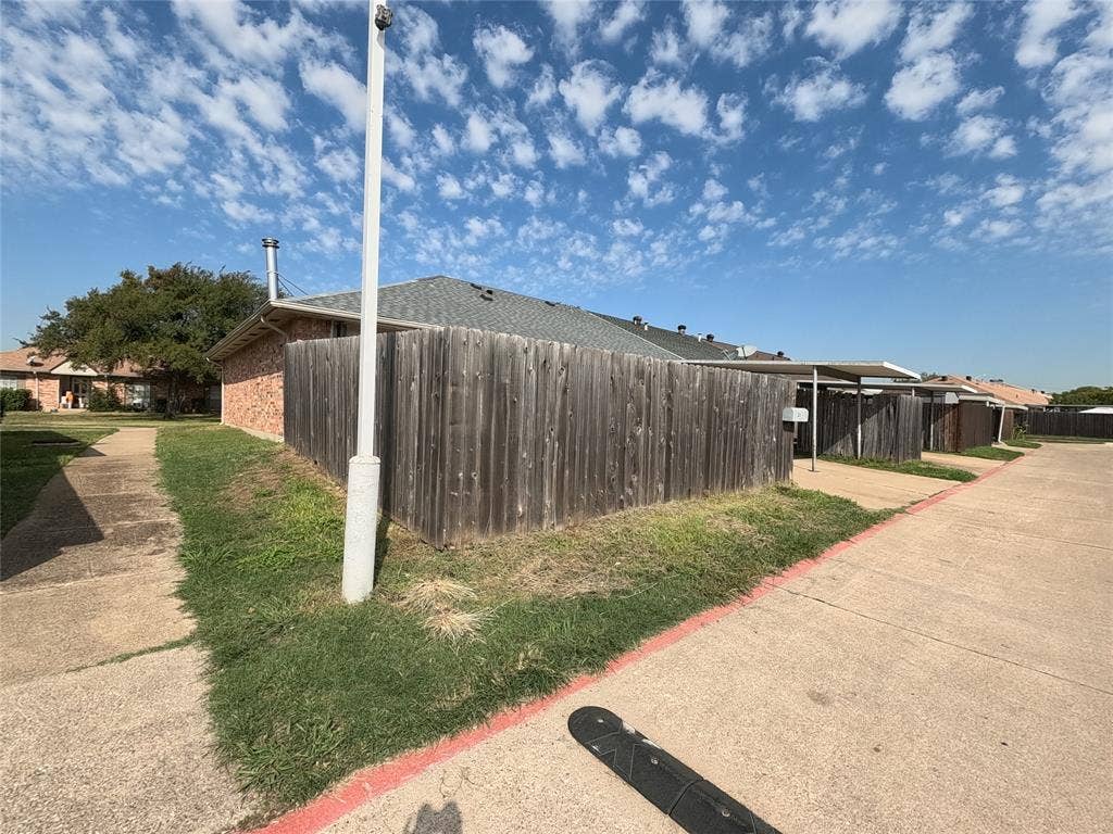 21 W Townhouse Lane, #33, Grand Prairie, TX 75052 Brick exterior with a gray shingle roof, wood privacy fencing, and multiple covered parking structures